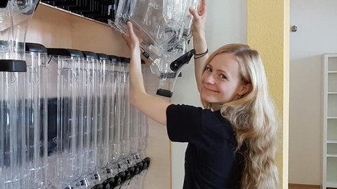 Frau mit langen blonden Haaren, die an einem Regal mit mehreren transparenten Röhren und schwarzen Elementen arbeitet.