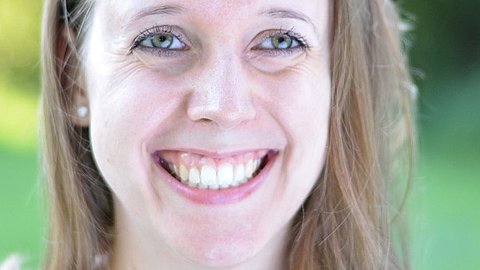 Frau mit langen blonden Haaren, trägt Perlenohrringe, vor grünem Hintergrund