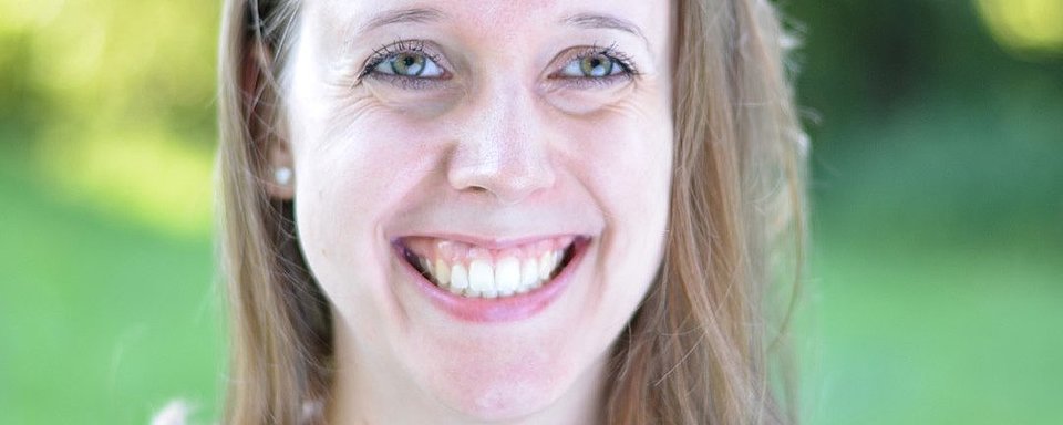 Frau mit langen blonden Haaren, trägt Perlenohrringe, vor grünem Hintergrund
